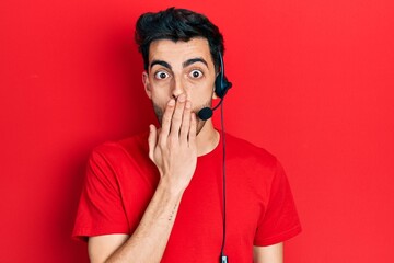 Young hispanic man wearing call center agent headset covering mouth with hand, shocked and afraid for mistake. surprised expression