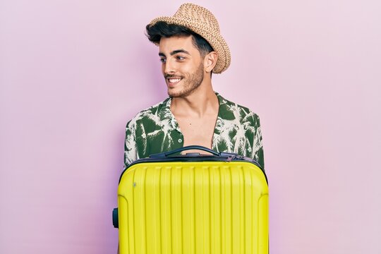 Young hispanic man wearing summer style and holding cabin bag looking to side, relax profile pose with natural face and confident smile.