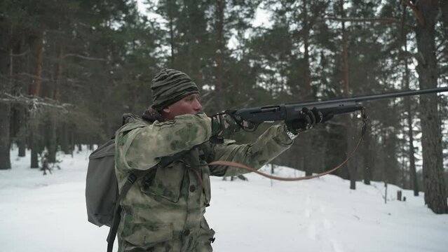 A hunter in camouflage clothing walks through the winter forest . A man removes a gun from his shoulder, preparing to shoot