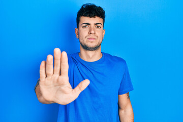 Young hispanic man wearing casual blue t shirt doing stop sing with palm of the hand. warning...