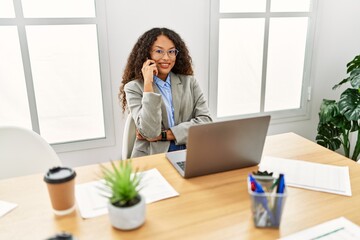 Young latin woman talking on the smartphone working at office