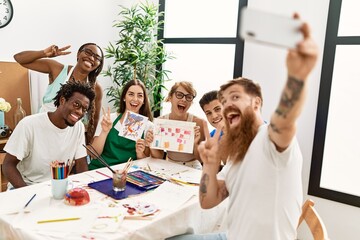 Group of people smiling happy make selfie by the smartphone sitting on the table at art studio.