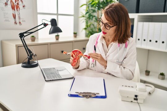 Young caucasian woman wearing doctor uniform holding anatomical model of uterus at clinic