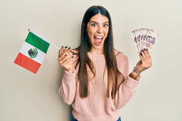 Young hispanic woman holding mexico flag and mexican pesos banknotes celebrating crazy and amazed for success with open eyes screaming excited.