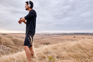 Jogger in headphones Check The Time Or Distance He Run, on Modern Smart Wristwatch, After Training, Dressed In Black Tracksuit, Looking At Side, In Field At Summer Morning, Alone