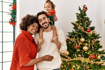 Couple and daughter smiling confident decorating christmas tree at home