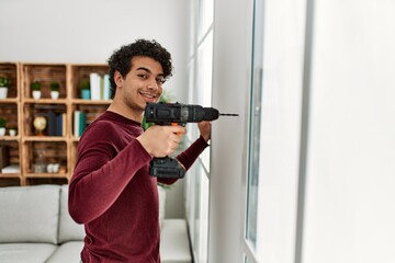 Young hispanic man smiling happy drillling wall at home.