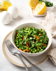 A bowl of salad with green peas, pickled carrots and parsley with olive oil on a bright kitchen table. Delicious healthy salad for health and weight loss closeup	