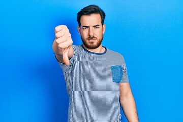 Handsome caucasian man with beard wearing casual striped t shirt looking unhappy and angry showing rejection and negative with thumbs down gesture. bad expression.