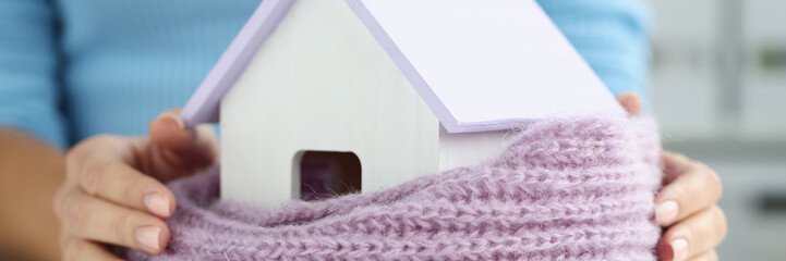 Woman wrapped small wooden house in warm scarf