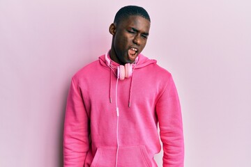 Young african american man wearing gym clothes and using headphones winking looking at the camera with sexy expression, cheerful and happy face.