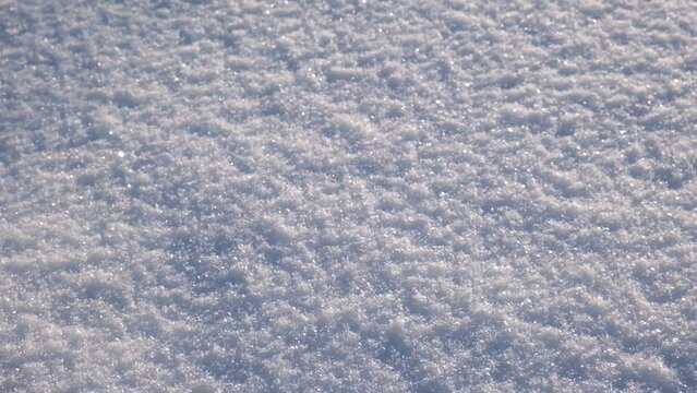 Snowy background. Smooth winter surface with a clearly expressed texture of snow in the morning sun. Snow covering in sunny day in slow motion panning. Natural snow texture. Snowy ground. Top view.