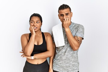 Young latin couple wearing sportswear standing over isolated background looking stressed and nervous with hands on mouth biting nails. anxiety problem.