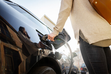 Cropped view of woman holds conector plugging in hands to recharge electric car.