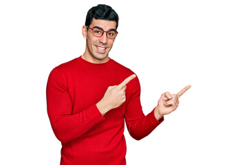 Handsome hispanic man wearing casual clothes and glasses smiling and looking at the camera pointing with two hands and fingers to the side.