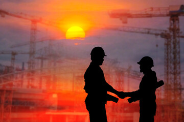 Silhouettes of male and female engineers shake hands to demonstrate cooperation with supervisors on construction site plans at sunset.