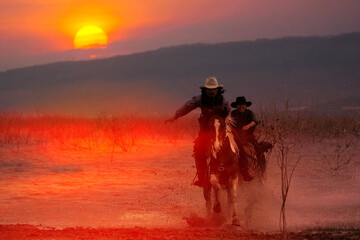 Silhouette of a cowboy riding a horse wading through the water at sunset behind a mountain.