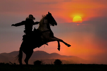 The silhouette of a cowboy riding a horse at sunset on the mountain