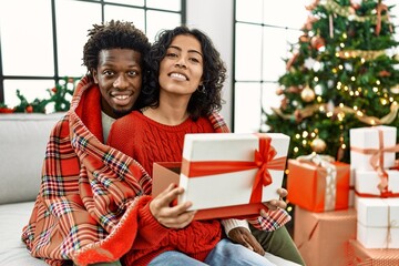 Young interracial couple smiling happy unboxing christmas gift sitting on the sofa at home.