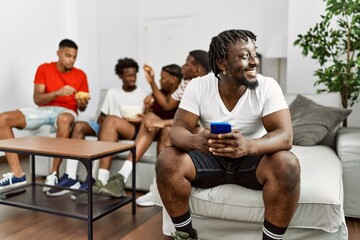 Obraz premium Group of african american people sitting on the sofa at home. Man smiling happy using smartphone.