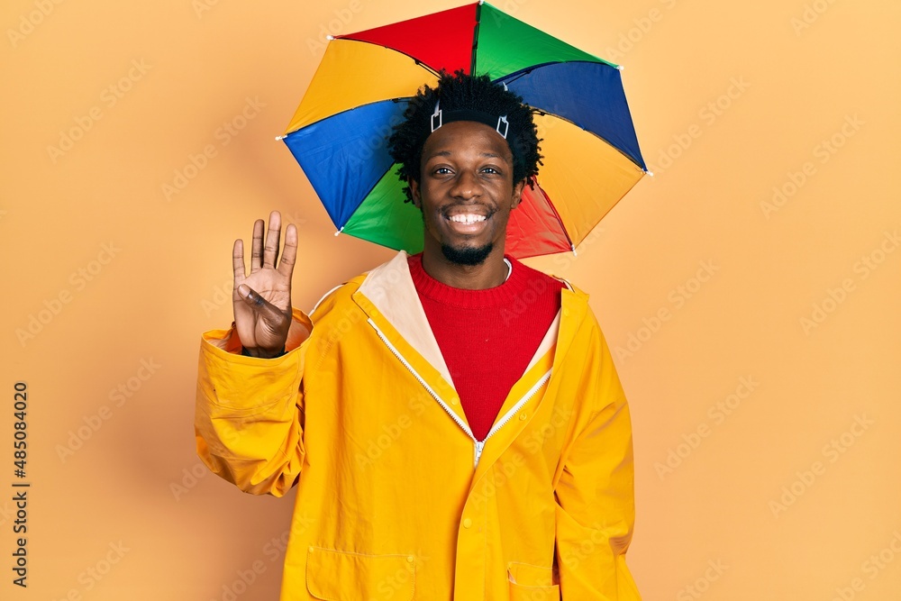 Poster Young african american man wearing yellow raincoat showing and pointing up with fingers number four while smiling confident and happy.