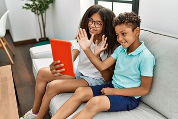 Brother and sister having video call using touchpad sitting on sofa at home