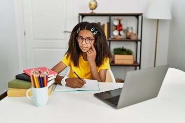 Young african american girl doing homework at home pointing to the eye watching you gesture, suspicious expression