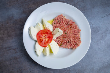 kibbeh dish with buffalo mozzarella and a slice of tomato, blue wooden base, viewed from above