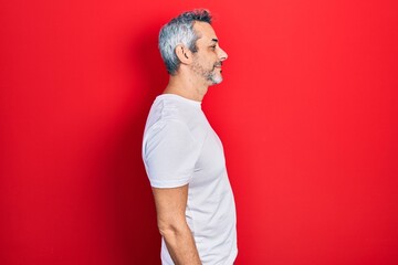 Handsome middle age man with grey hair wearing casual white t shirt looking to side, relax profile pose with natural face with confident smile.