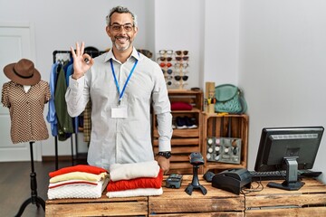 Middle age hispanic man working as manager at retail boutique smiling positive doing ok sign with hand and fingers. successful expression.