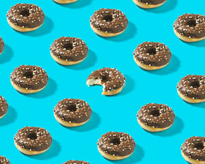 Creative trendy pattern with chocolate donuts and one donut bitten into on bright blue background.