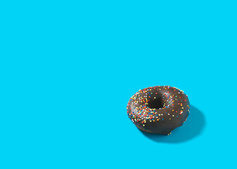 Single chocolate donut with colorful sprinkles on bright blue background with copy space.