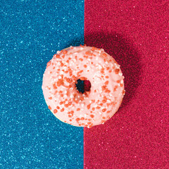 Creative composition with single pink donut on duo tone glitter blue and red background.
