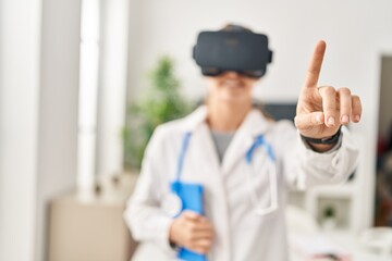 Young blonde woman wearing doctor uniform using touchpad and vr goggles at clinic