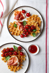 Belgian potato savory waffles with prosciutto, cherry tomatoes, basil leaves and hot tomato jam or spicy sauce. Served breakfast, brunch on light background