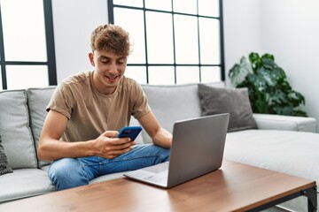 Young caucasian man smiling confident using laptop and smartphone at home