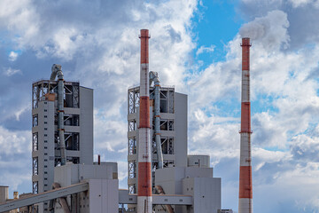 Industrial cement production facilities with tall pipes against a bright blue sky and white clouds