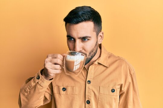 Handsome hispanic man enjoying a cup of coffee over yellow background
