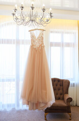 Luxury wedding dress hanging on the chandelier in a hotel room. Bridal gown. Wedding