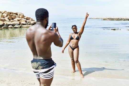 Young african american man making photo to woman using smartphone at the beach.