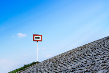 Black arrow on white background and in red frame standing atop of cobblestone paved hill at day. Blue sky with great clouds. Copy space, concept