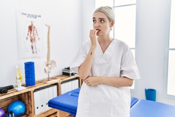 Young caucasian woman working at pain recovery clinic looking stressed and nervous with hands on mouth biting nails. anxiety problem.