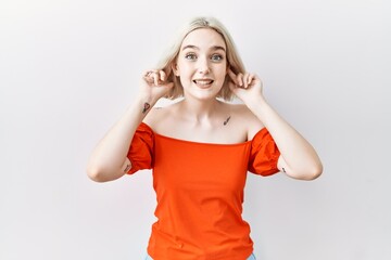 Young caucasian woman standing over isolated background smiling pulling ears with fingers, funny...