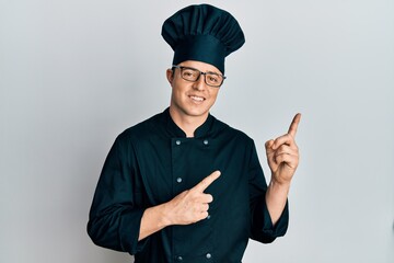 Handsome young man wearing professional cook uniform and hat smiling and looking at the camera...