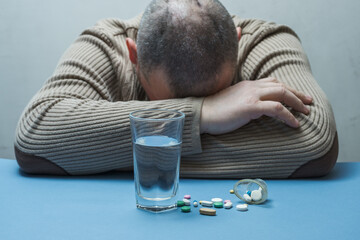 The man hides his face, medical preparations are on the table in front of him.
