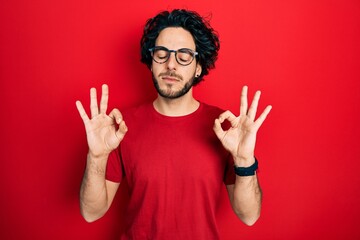 Handsome hispanic man wearing casual t shirt and glasses relax and smiling with eyes closed doing meditation gesture with fingers. yoga concept.