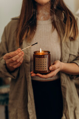 A young woman holds a burning candle with an advent calendar on her. The girl set fire to a christmas candle. Big match with a candle in a jar in female hands.