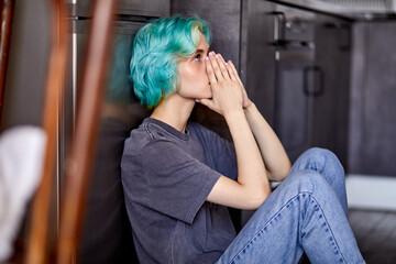 Depressed female upset with something, sitting alone on floor in kitchen. Attractive unhappy woman...