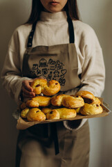 Young woman in the kitchen apron holds a tray with buns in her hands. Saffron buns in female hands....