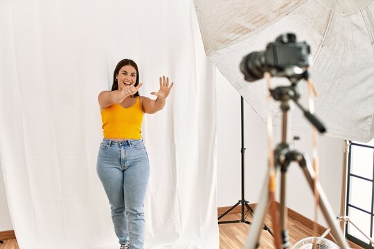 Young beautiful hispanic woman posing as model at photography studio showing and pointing up with fingers number six while smiling confident and happy.